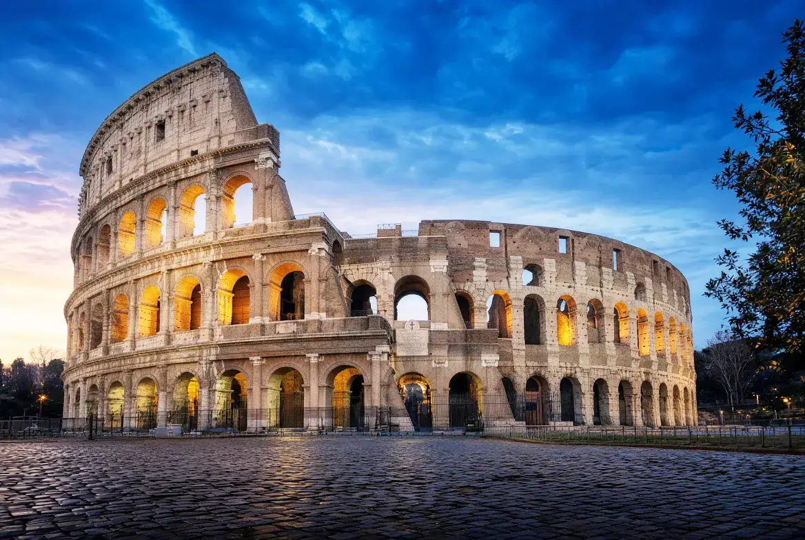 Exterior of the Colosseum at dusk, with warm light inside the arches. ©2026 SafarbazTravel.com™